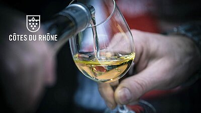 一杯白葡萄酒从带有罗纳河谷标志的酒瓶中倒出，特写镜头展示了葡萄酒的品质。这张图片强调了罗纳河谷葡萄酒的真实性和高端品质，这些葡萄酒通过科卫宝SCRIBOS 防伪解决方案得到保护，同时为消费者提供互动平台以获取更多信息。