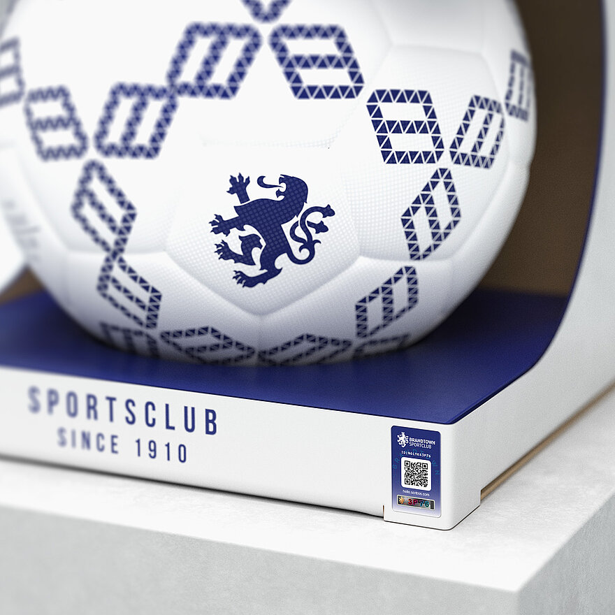 一个印有蓝色几何图案和狮子徽章的白色足球，包装上印有“Sportsclub Since 1910”字样。足球采用激光光刻VeoMark®技术，集公开和隐蔽防伪功能于一体，可有效防止假冒。该解决方案可确保产品真实性，提升品牌信任度。