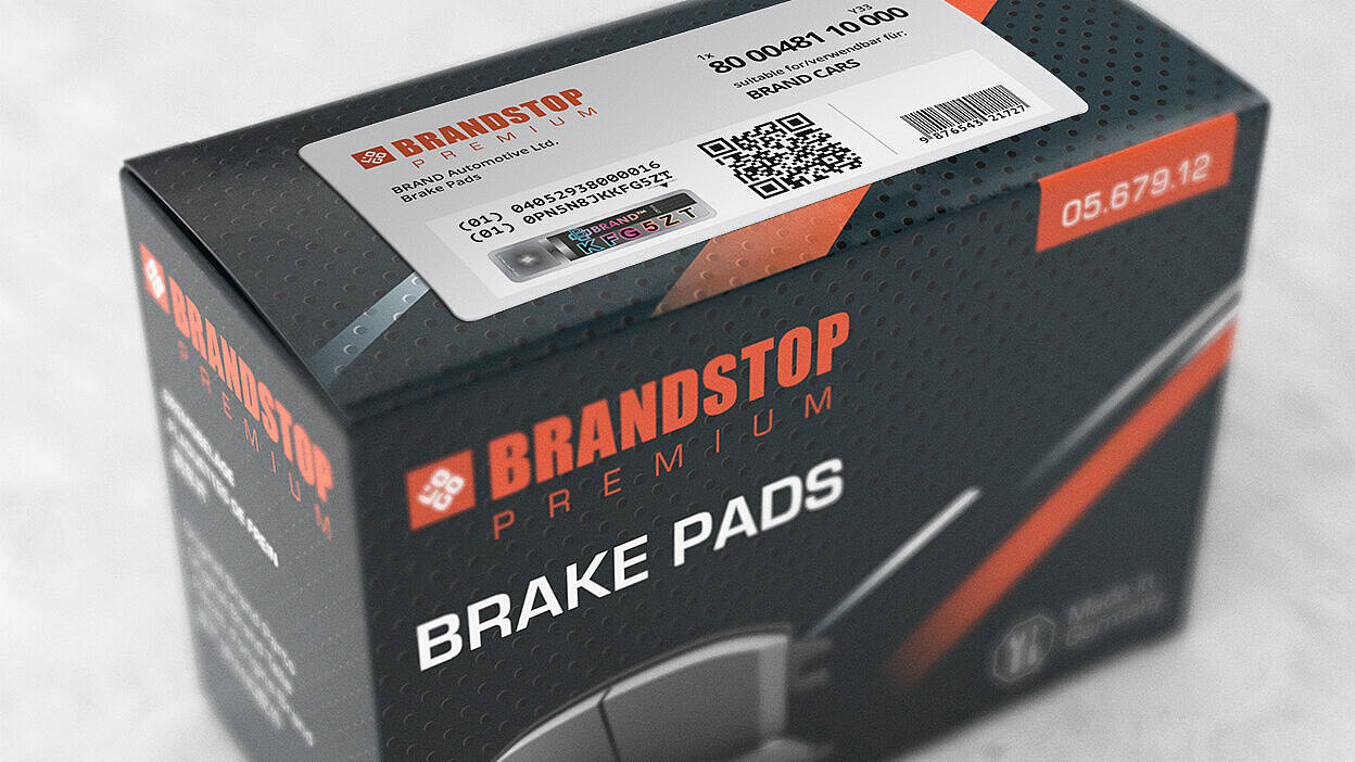 一个装有Brandstop高级刹车片的矩形盒子,表面贴有防伪标签。标签上印有二维码、产品信息以及独特的防伪元素,在激光光刻VeoMark®品牌下,全息设计展示了彩色字母数字字符(KFG5ZT)。该标签展示了先进的防伪技术,结合了公开和隐蔽的安全功能。